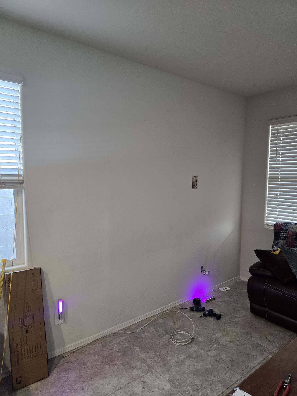 An empty living room wall with outlets and tools before the television was mounted